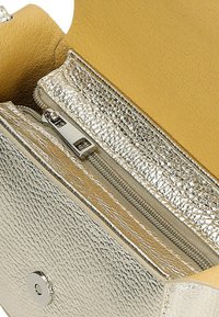 Zilveren metallic portemonnee met textuur aan de buitenkant, gele binnenkant, ritsvak en drukknoopsluiting. Bevat zowel gladde als gemusterde materialen.