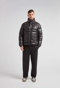 Sort pufferjakke med høj krave, blank finish, lynlås foran og to lommer. Sammen med sorte bukser og sneakers med hvide detaljer.