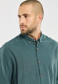 Türkises Hemd mit durchgehender Knopfleiste aus weichem Stoff und Kent-Kragen, ausgestattet mit braunen Knöpfen und einer lockeren Passform. Einfaches Design mit glatter Textur.