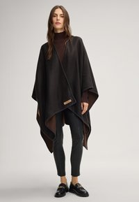 Donkerbruin poncho met een contrasterende binnenlaag, afgewerkt met contrasterende stiksels en een merklabel. Draag het over een aansluitende turtleneck en broek.