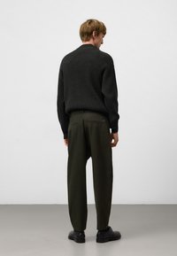 Donkergrijze geribbelde trui met een relaxte pasvorm, gecombineerd met losse donkergroene broek. Zwarte schoenen maken de look compleet.