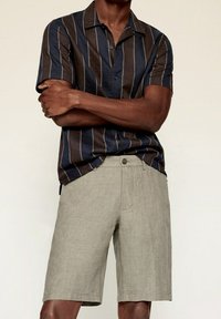 Camisa de manga corta con rayas verticales en azul marino y marrón, combinada con pantalones cortos de lino gris claro. Cuenta con cuello y cierre de botones.