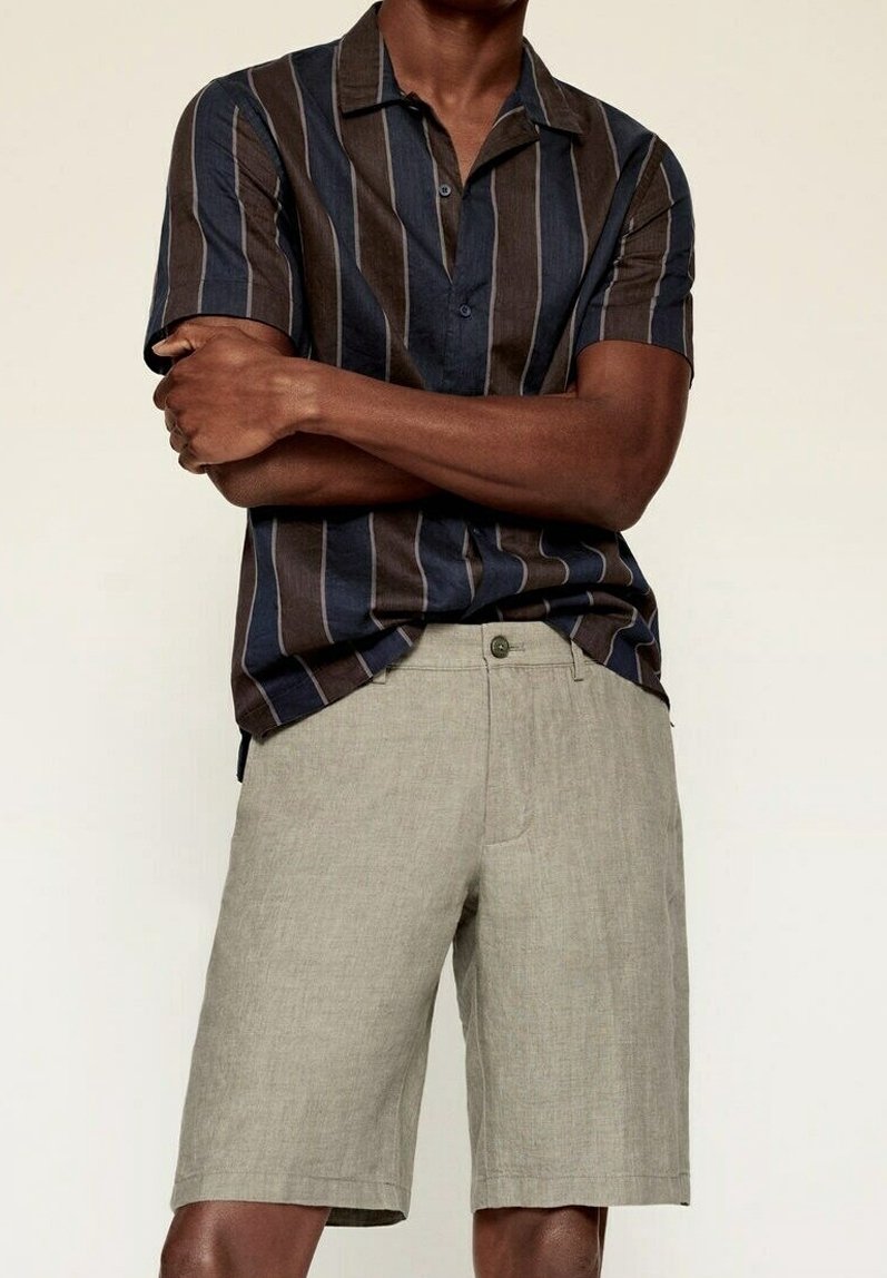 Camisa de manga corta con rayas verticales en azul marino y marrón, combinada con pantalones cortos de lino gris claro. Cuenta con cuello y cierre de botones.