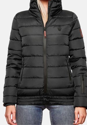 Czarna pikowana kurtka z kapturem, zamkiem z przodu i zapinanymi na zamek kieszeniami, noszona na niebieskich jeansach, pokazująca górną część ciała i dłonie.