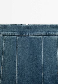 Tissu en denim bleu avec des coutures verticales, suggérant le haut d'une jupe ou d'un pantalon sur un fond blanc.