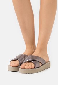 Sandales glissantes en bronze pailleté avec un design de lanière entrecroisée et une semelle épaisse beige, présentant un fond texturé pour une meilleure adhérence.