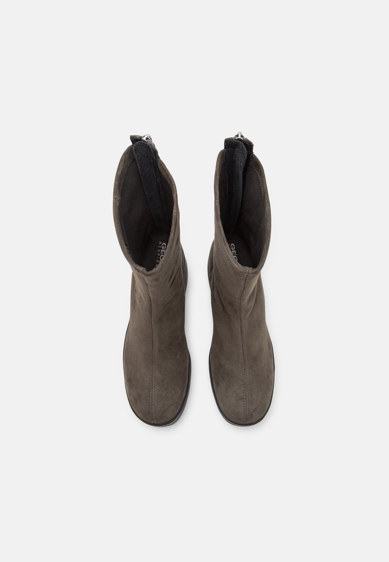 Bottines en daim gris avec une texture lisse, dotées d'une fermeture éclair à l'arrière et d'une doublure en tissu doux, conçues pour un enfilage facile.