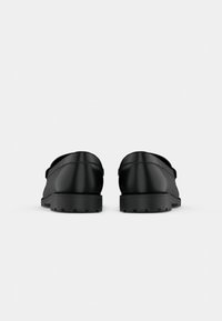 Paire de mocassins en cuir noir avec semelles en caoutchouc épaisses et texturées, vus de dos sur un fond blanc uni.