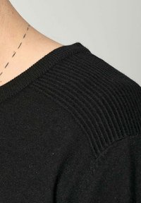 Pull en maille noir avec un col rond et des accents côtelés sur les épaules, mettant en avant une texture douce et une silhouette ajustée.