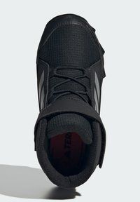 Black athletic shoe featuring a textured upper, lace closure, adjustable strap, and rubber sole with traction studs. Silver detailing on sides.