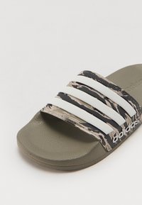 Adidas sandal med et kamuflasjemønster i beige og grønt med tre hvite striper, og en teksturert olivengrønn såle.