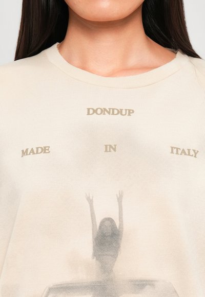 Camisa beige con el texto "DONDUP MADE IN ITALY" y una imagen desvanecida de una persona levantando los brazos mientras está sentada en el techo de un coche.
