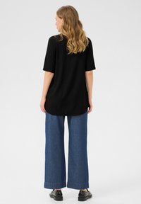 Top nero a maniche corte con vestibilità morbida, abbinato a pantaloni in denim blu a gamba larga con orli risvoltati e calzature nere.