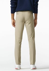 Beige chino's met een rechte pasvorm, voorzien van twee achterzakken met knopen. Het materiaal lijkt glad en wordt gecombineerd met witte sportieve schoenen.