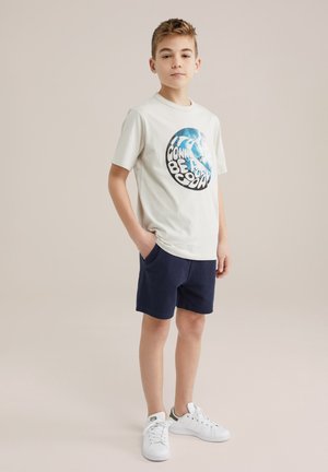 Maglietta grigia chiara a maniche corte con una stampa grafica colorata; abbinata a pantaloni corti blu scuro e sneaker bianche. Entrambi i capi sono casual e comodi.