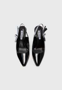 Escarpins en cuir verni noir avec une pointe effilée, présentant une texture lisse et des rubans décoratifs griffés en noir et blanc.
