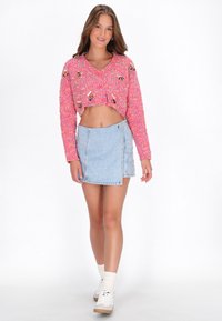 Grezna rozā adīta augšdaļa ar krāsainiem ziedu rotājumiem, apvienota ar džinsu apakšsvārku un baltām sporta kedām ar krēmkrāsas zeķēm.