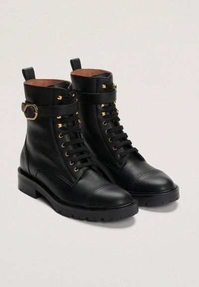 Črne usnjene gležnjarje z zlatimi dodatki, okroglo konico, vezalni sprednji del in širok trak z zaponko okoli gležnja.