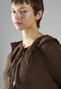 Brauner Strickpullover mit strukturiertem Finish, mit Kapuze, Schnüredetails am Ausschnitt und leichten Fransen an den Kanten.