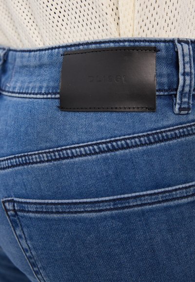 Tume sinine denim teksad, millel on must naha silt "DL1961" seljaosa vööl. Nähtavad õmblused ja tasku detailid.