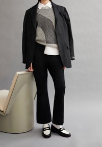 Zwarte op maat gemaakte blazer over een gestreept breisweater, wit shirt en zwarte broek. Zwart-witte loafers maken de outfit af.