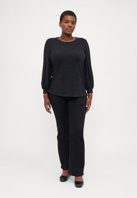 Black top with textured fabric, featuring puffed sheer sleeves, paired with black flared pants and black flat shoes. Simple, elegant silhouette.
