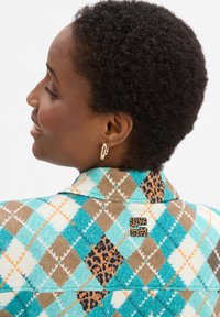 Multifarbige Jacke mit einem geometrischen Muster in Aquablau, Braun und Orange, mit einem Leopardenmuster-Akzent und einem Markenpatch auf dem Rücken.