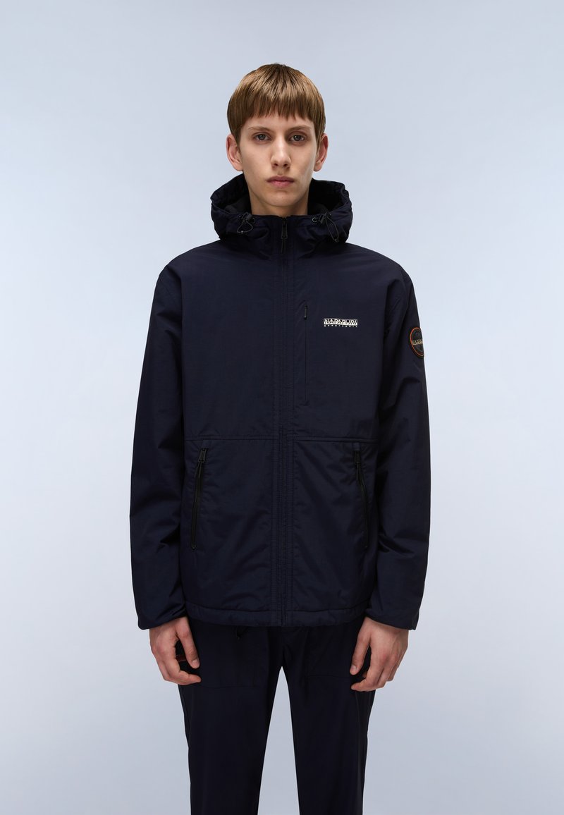 Giacca impermeabile blu navy con cappuccio, tasche con zip, logo sul petto e polsini elasticizzati, caratterizzata da una texture liscia e opaca.