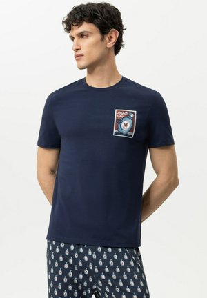 Mann trägt dunkelblaues T-Shirt mit Ahornsirup-Flaschen-Aufnäher und passende dunkelblaue Shorts mit kleinem Muster von Ahornsirup-Flaschen.