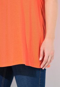 Oranžové bavlněné tričko s rovním lemem, bočními rozparky a krátkými rukávy, doplněné tmavě modrými riflovými džíny s hladkou texturou.