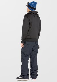 Black hoodie with a drawstring, paired with loose-fitting dark blue pants. Wearing a blue patterned beanie and black sneakers.
