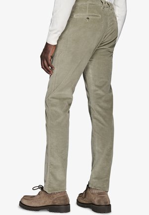 Pantaloni in velluto a coste verde chiaro con vestibilità dritta, dotati di una tasca posteriore e una sottile texture verticale. Indossati con scarpe marroni con lacci.