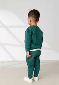 Grüne Sweatshirt- und Hosenkombination aus Baumwolle, mit gerippten Bündchen und einem weißen Taillenbund, kombiniert mit weißen Sneakern.