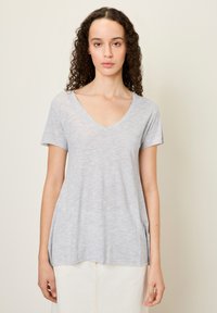 Pilkas, trumpas rankovėmis V-nesmuklis marškinėliai, pagaminti iš minkštos, lengvos medžiagos, su atsipalaidavusiu siluetu ir apvaliu sijonu, pasižymintys subtiliais tekstūros pokyčiais.