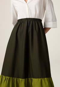 Gonna nera con vita elastica e orlo arricciato verde, abbinata a una camicia bianca con bottoni. Presenta un tessuto morbido e leggero.