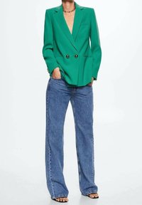 Groene dubbelgeknoopte blazer met gouden knopen, slim fit en notch revers, gecombineerd met losse blauwe denim jeans en zwarte sandalen.
