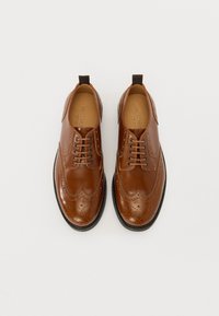 Brązowe skórzane buty z wzorem na wingtips, z dekoracyjnymi perforacjami, gładką powierzchnią, sznurowadłami i czarną podeszwą.