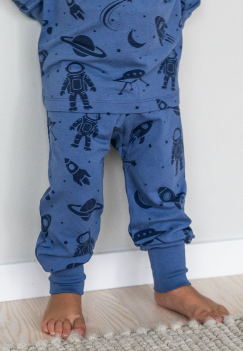 Blå tvådelade pyjamaser med ett rymdtema som har astronauter, raketer och planeter i mörkblått på ett ljusblått tyg.