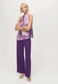Haut sans manches en tissu dégradé violet et rose ; associé à un pantalon large violet ; modèle portant des bracelets en argent et des sandales.