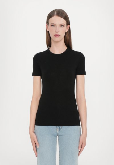 T-shirt noir à manches courtes en tissu lisse, avec un col rond et une silhouette ajustée, associé à un jean bleu clair.