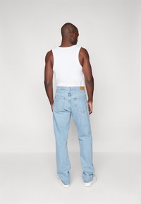 Lyseblå denimbukser med en afslappet pasform, der har et brun læderlap ved taljen og en standard baglomme-design.