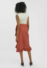 Beżowy, żeberkowany top na ramiączkach w połączeniu z miedzianą spódnicą midi z falbaniastym dołem i bocznym detalem w postaci kokardy. Gładka tekstura, swobodny krój.