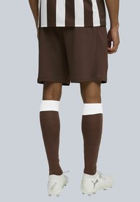 Brune træningsshorts med en hvid og brun stribet trøje, parret med brune knælange sokker og hvide fodboldstøvler.