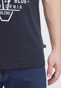 Tmavě modré bavlněné tričko s kulatým nákrčníkem, s bílým potiskem textu "California Blend" a malou logovou nášivkou na levé straně.