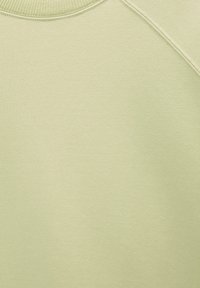Tissu vert clair en gros plan montrant une texture lisse et des détails de couture près d'un col arrondi.
