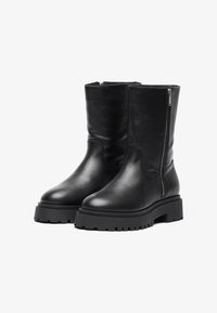 Botas de tobillo de cuero negro con una textura suave, cierre de cremallera lateral y una suela de goma gruesa con un patrón de relieve para mayor agarre.