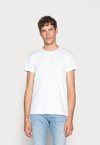 Weißes Baumwoll-T-Shirt mit kurzen Ärmeln, Rundhalsausschnitt und geradem Schnitt, kombiniert mit hellblauen Jeans. Schlichtes Design, keine sichtbaren Muster.