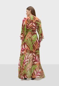 Robe longue et transparente de couleur marron avec des motifs de feuilles vibrants en vert, rose et orange. Manches évasées et ceinture croisée à la taille.