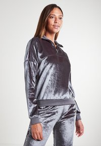 Felpa quarzi-zip in velluto grigio scuro, caratterizzata da una texture morbida, polsini e orlo a coste, e dettagli accentuati sulle spalle.