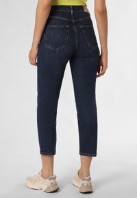 Jeans scuri, a vita alta, con gamba affusolata, design a cinque tasche e leggeri dettagli di sbiadimento. Abbinati a sneakers chiare.